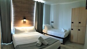 Una habitación de hotel con una cama grande, otra más pequeña, un armario y una lámpara de pared.