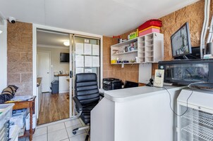 Um escritório compacto com cadeira de escritório preta, mesa branca, computador, impressora e uma pequena geladeira.