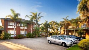 Un hotel con zona de estacionamiento, palmeras y cielo despejado.