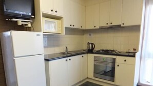 Una cocina compacta con armarios blancos, microondas integrado, estufa a gas y horno de acero inoxidable.