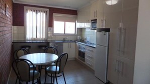 Una cocina compacta con una mesa redonda y sillas, un refrigerador, un microondas y una ventana con persianas.