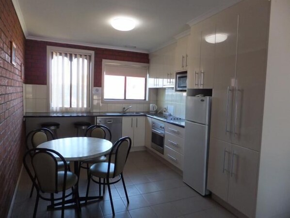 Una cocina compacta con una mesa redonda y sillas, un refrigerador, un microondas y una ventana con persianas.