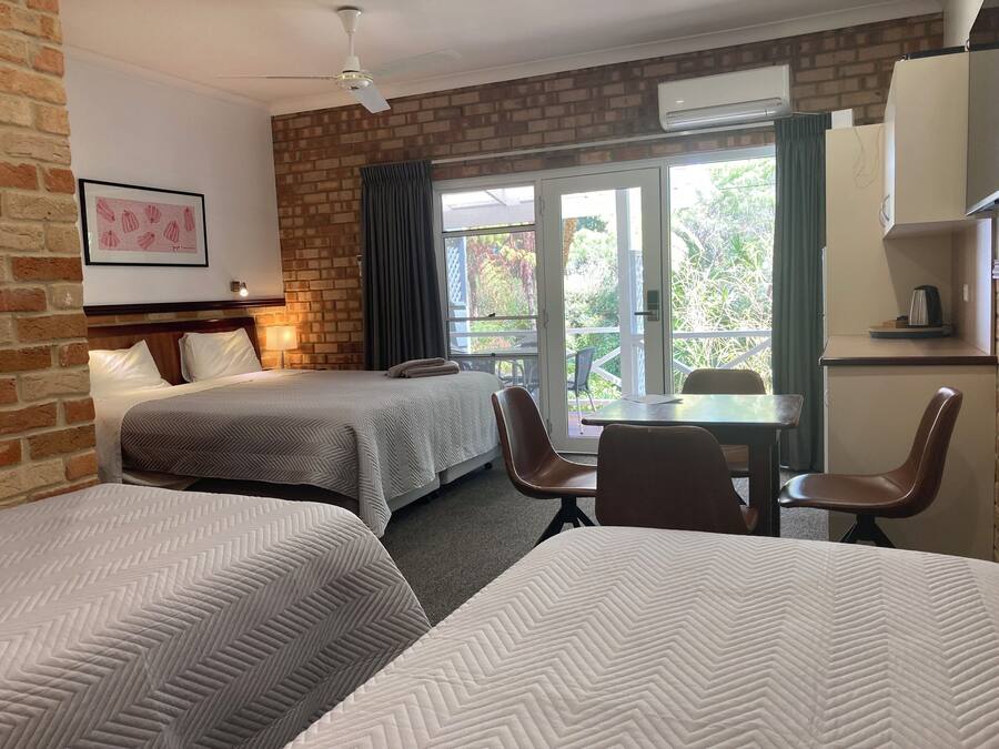 Une chambre d’hôtel avec deux lits, une table à manger, des chaises, un ventilateur de plafond et une fenêtre avec des rideaux.