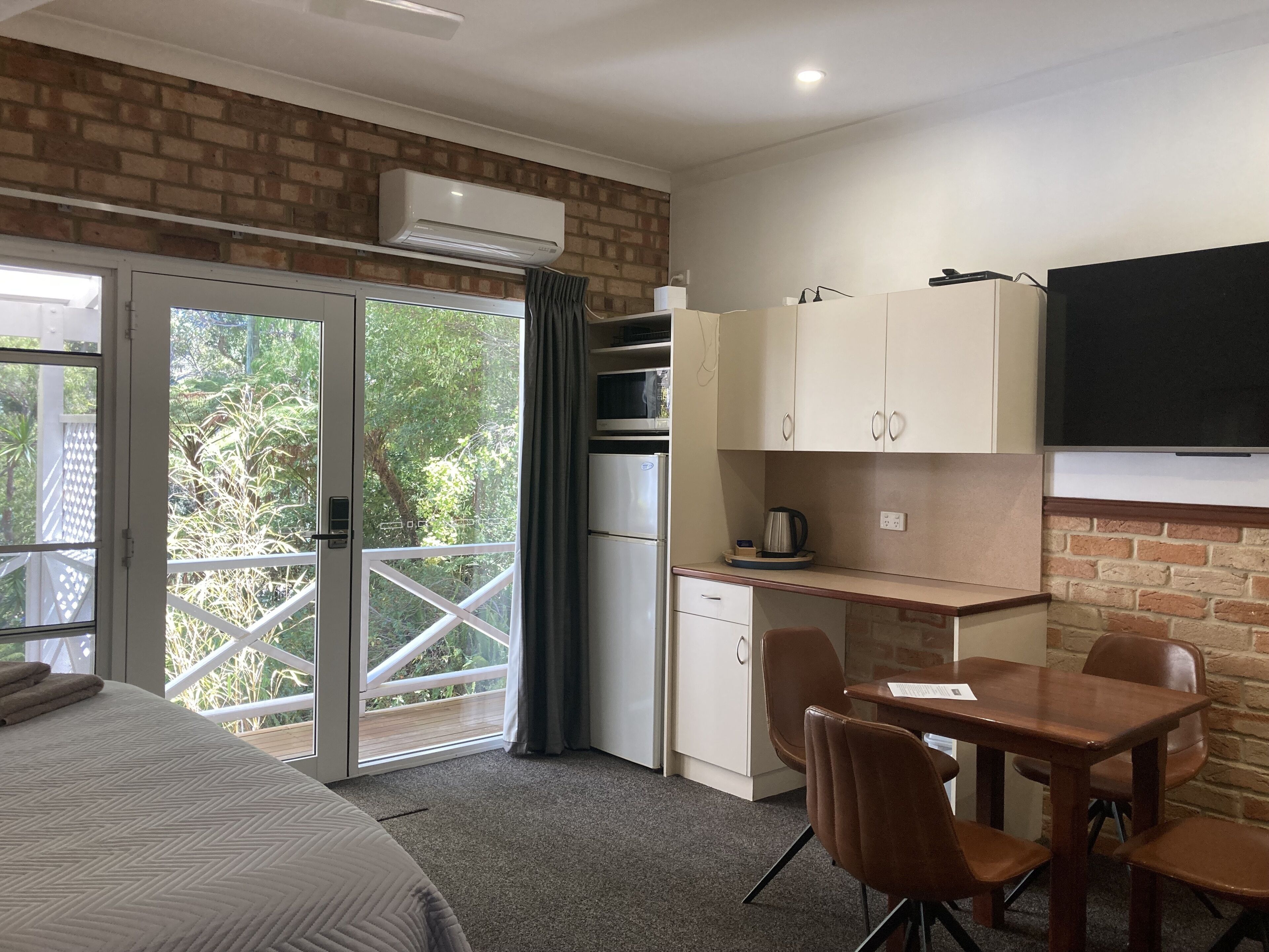 A compact room with a bed, a kitchenette, a dining area, and a sliding glass door leading to a balcony.