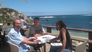 A dining area with a view of the ocean, featuring outdoor seating and a wooden deck. - Edge of the Forest (Margaret River)