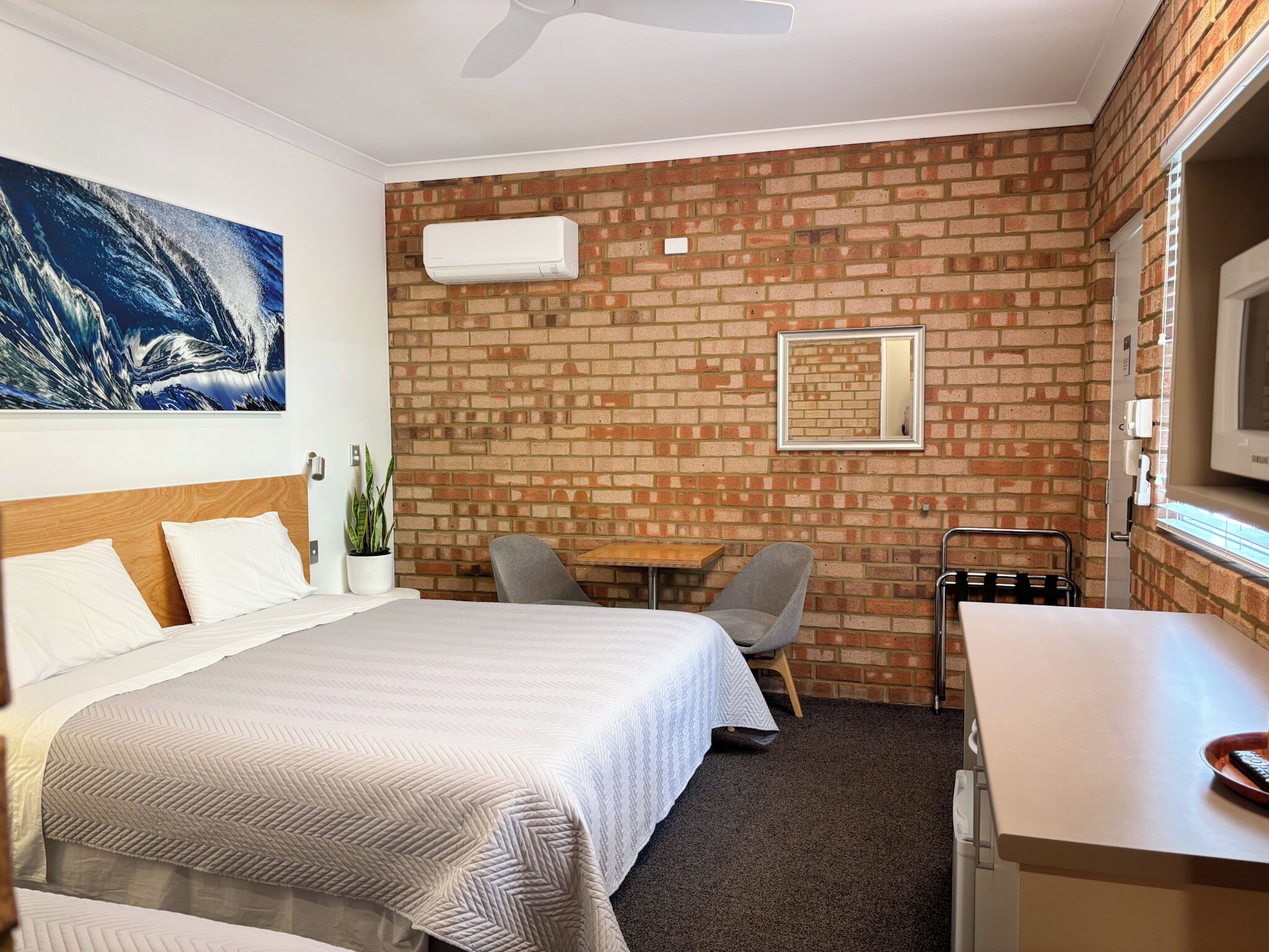 Hotelkamer met een bed, een bureau, een stoel, een televisie en een bakstenen muur.