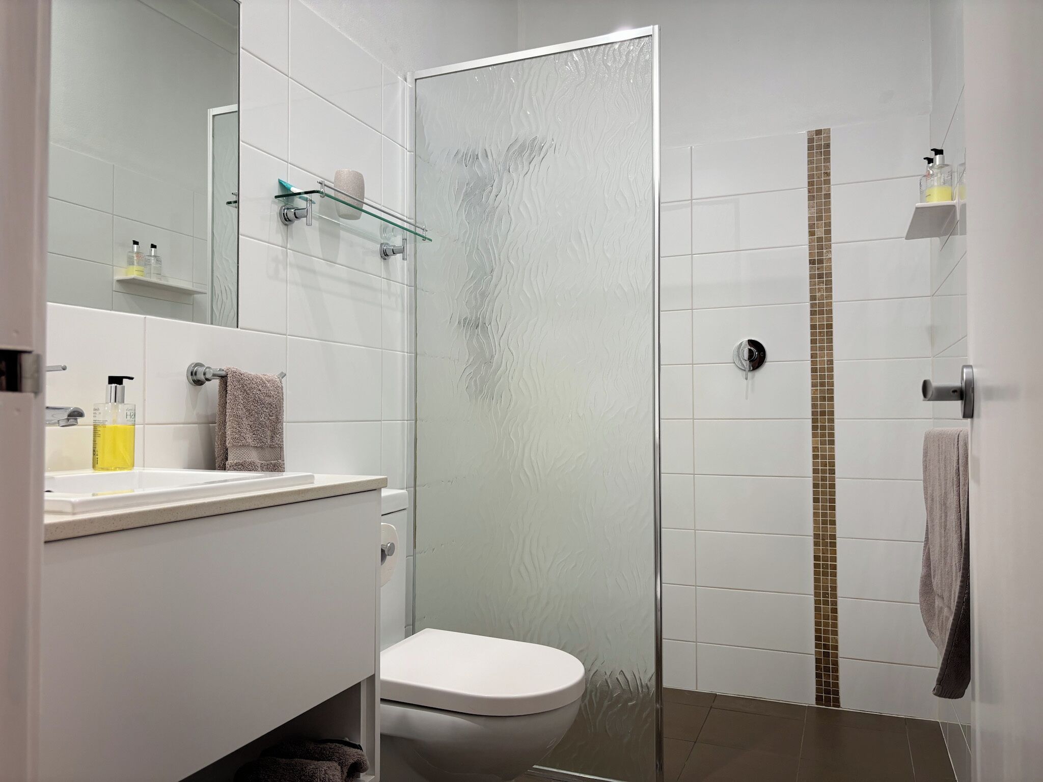 Un bagno moderno con cabina doccia in vetro, un water bianco e un lavabo con articoli da toilette.