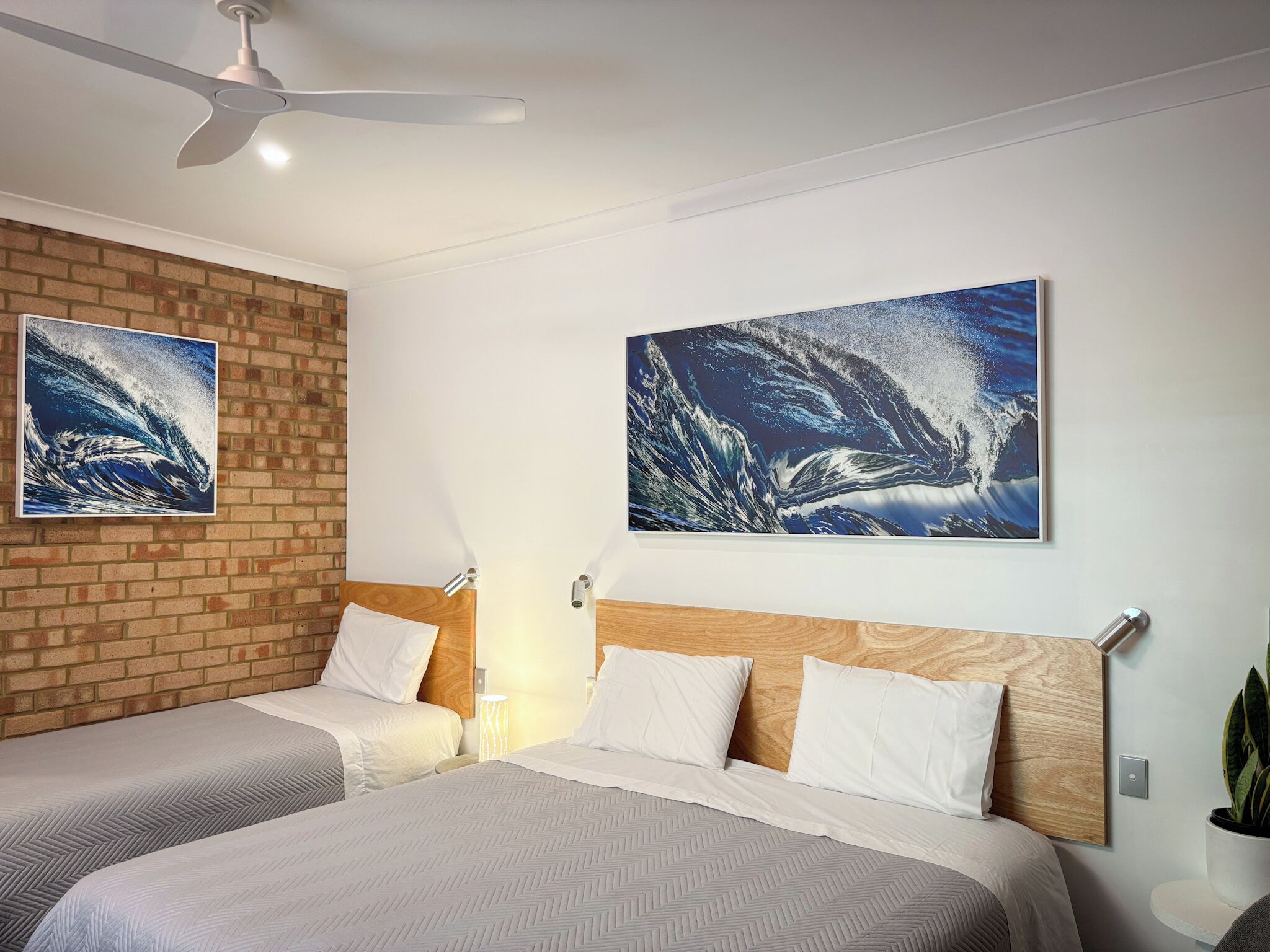 Ett hotellrum med två sängar, en tegelvägg och två stora tavlor som föreställer havsvågor.