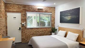 A bedroom with a brick wall, a window with blinds, a bed with white bedding, a ceiling fan, and a wall-mounted artwork.