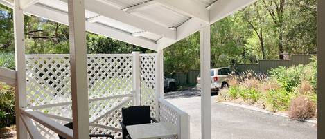A covered outdoor seating area with a white lattice partition, a table, and two chairs.