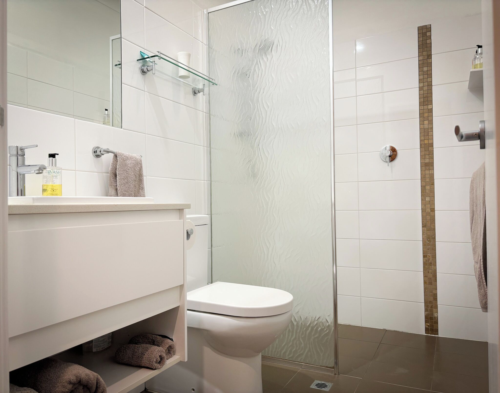 Un baño moderno con inodoro, cabina de ducha de vidrio y tocador con espejo.