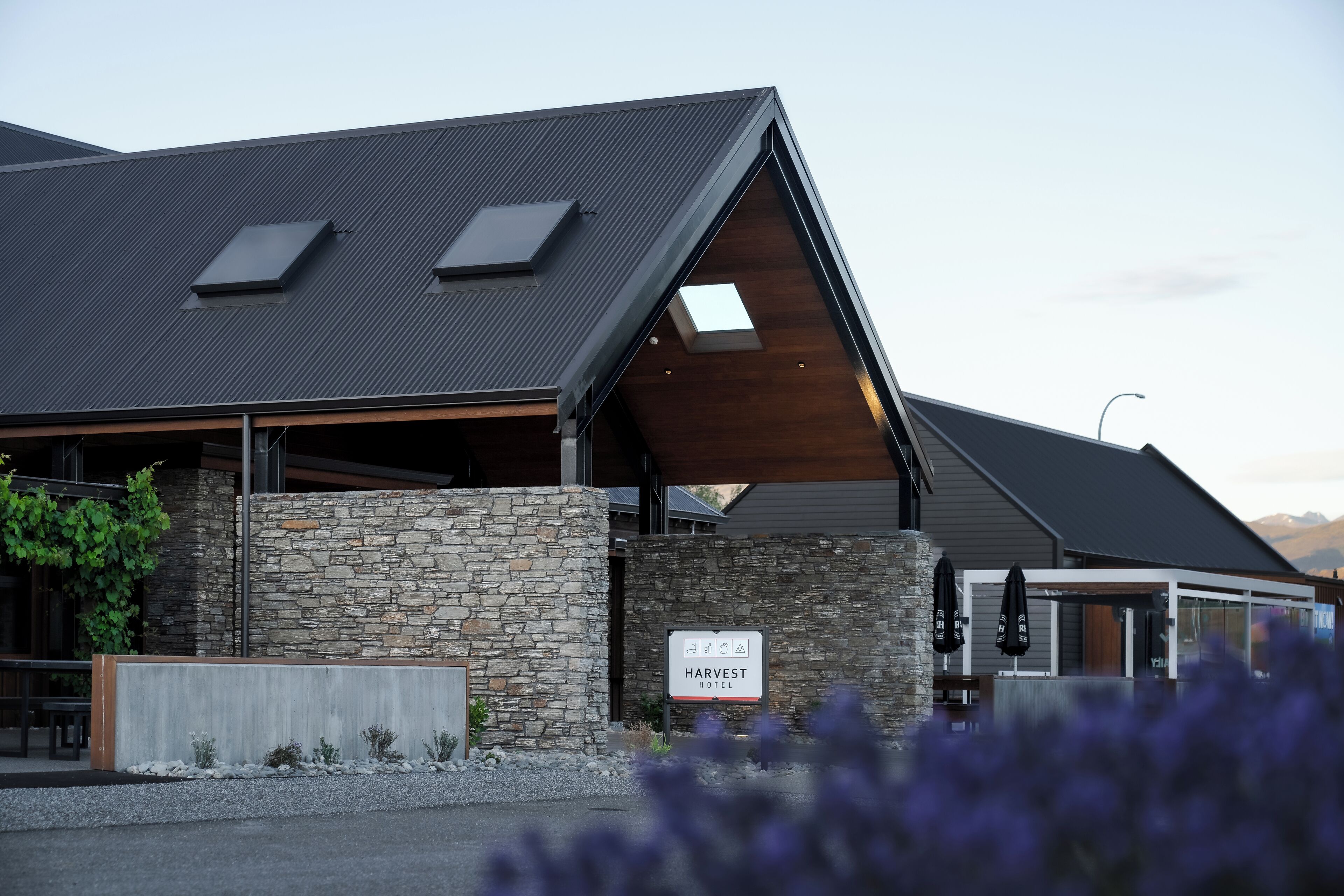 A modern building with a stone facade, a sign reading "HARVEST HOTEL," and a covered outdoor seating area.