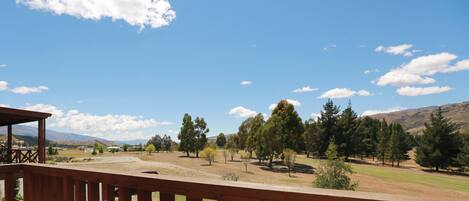 A wooden deck overlooking a grassy area with trees and mountains in the background.