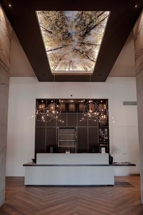 A modern reception area with a large digital display of trees, a reception desk, and a hanging light fixture. - Harvest Hotel (Cromwell)