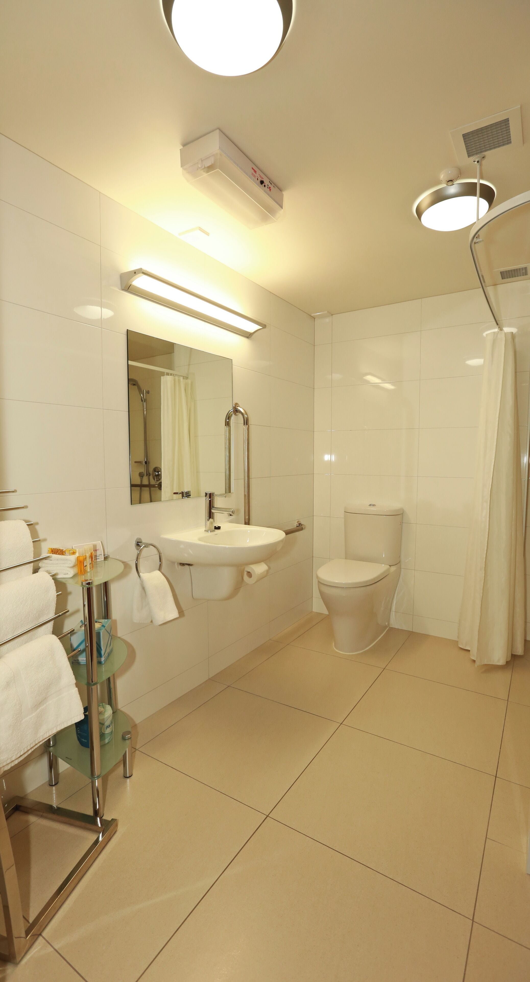 Une salle de bain moderne avec une étagère en verre où sont rangés les articles de toilette, un lavabo, des toilettes et un espace douche.