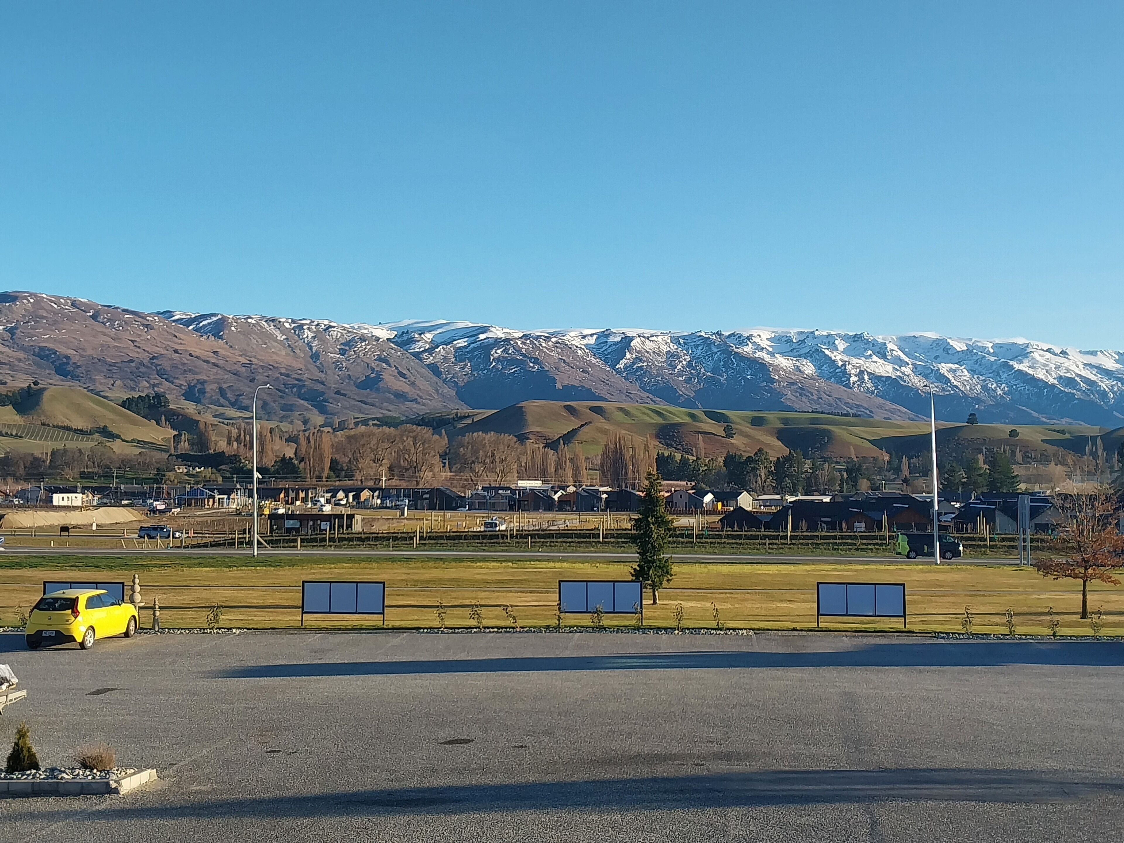 A parking lot with a yellow car, a small tree, and a mountain range in the background.