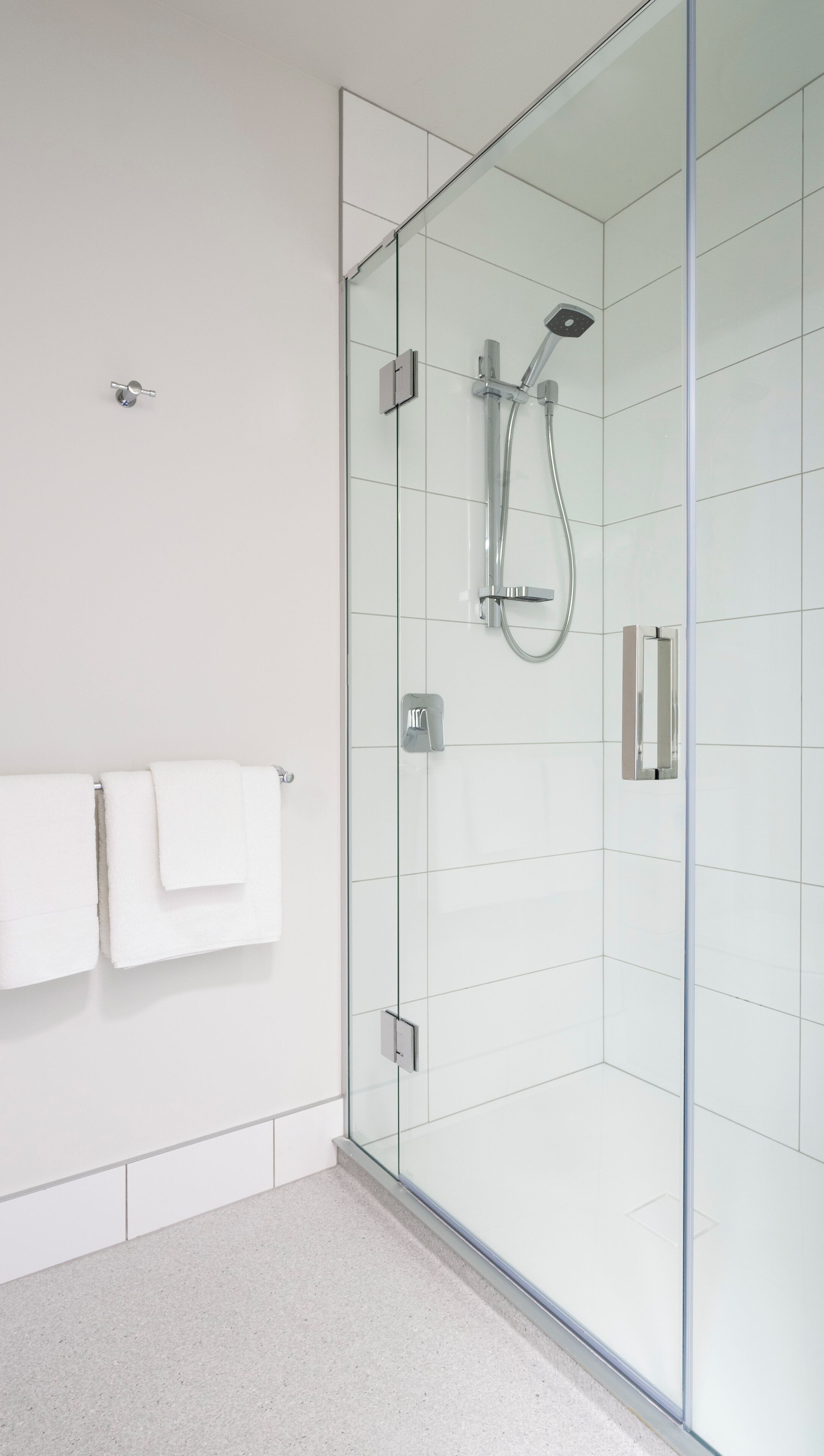 A modern bathroom with a glass shower enclosure, a towel rack with white towels, and a tiled floor.