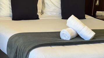 Una cama bien hecha con ropa de cama blanca y gris oscuro, una manta gris y dos toallas blancas enrolladas.