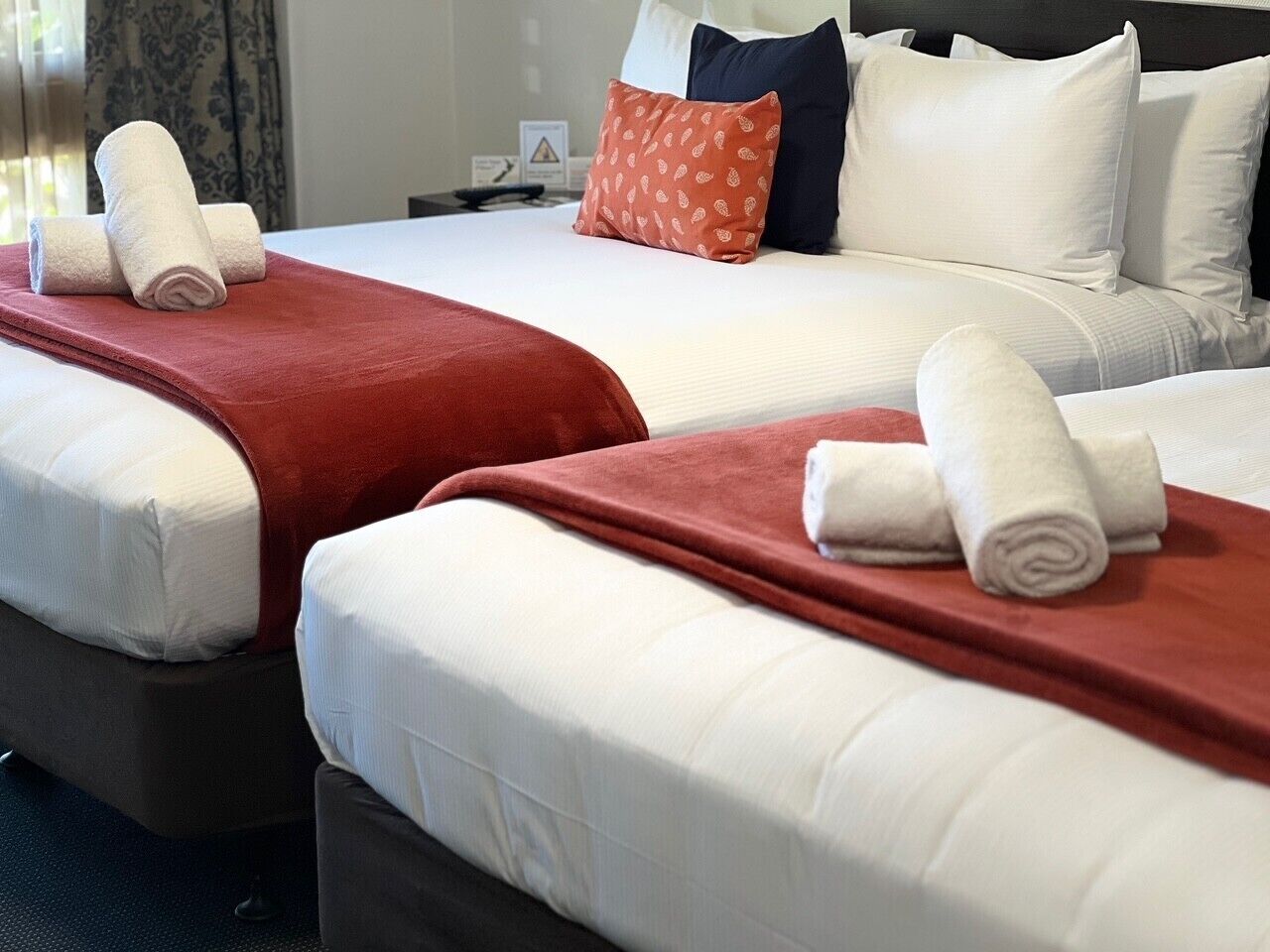 A hotel room with two beds, each with white linens and red blankets.