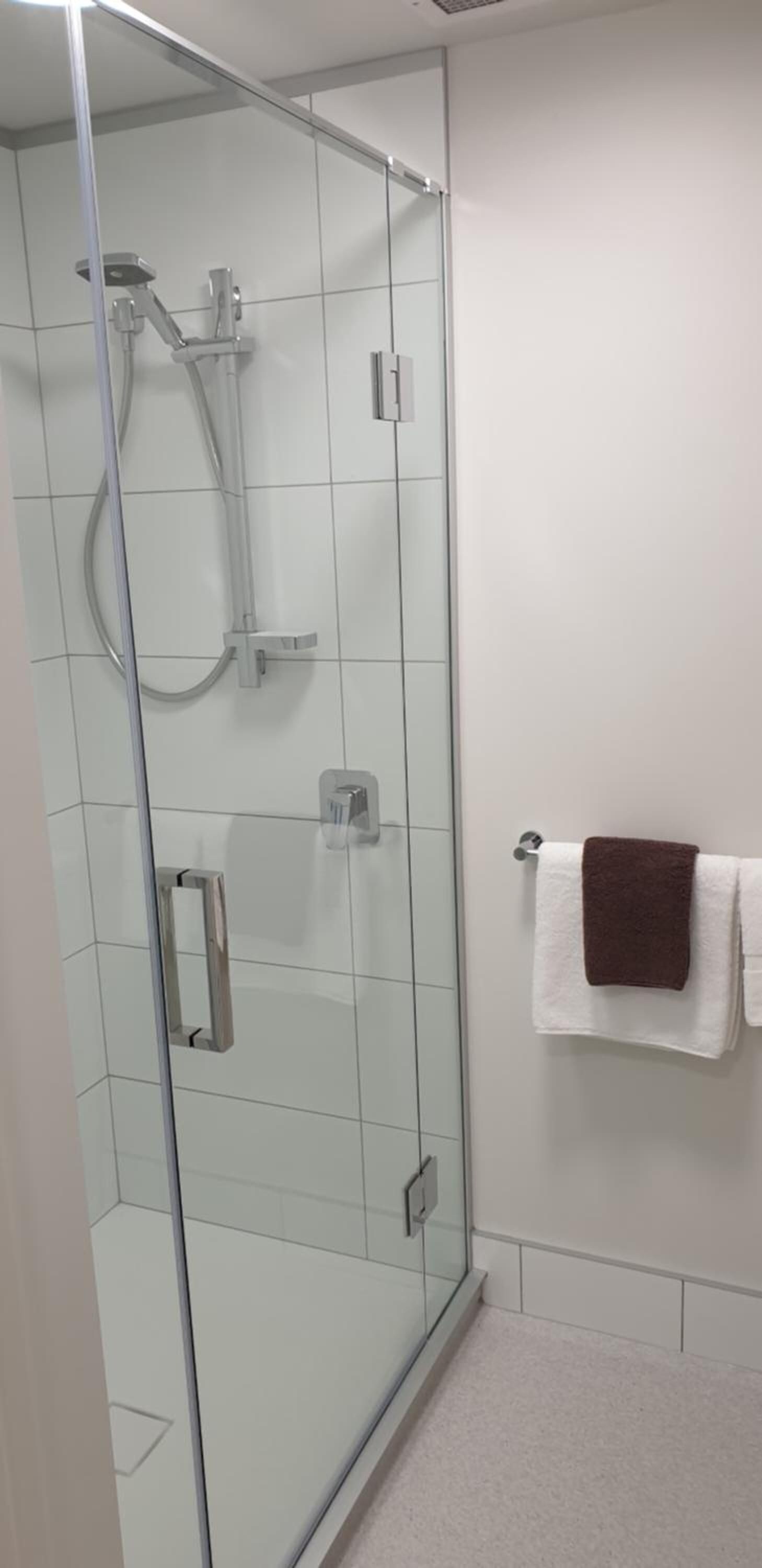 A glass-enclosed shower with a handheld showerhead and a wall-mounted faucet.
