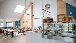 A café with a central counter displaying baked goods, wooden walls, and a view of the outdoors. - Harvest Hotel (Cromwell)