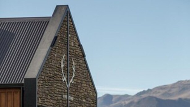 A modern building with a sloped roof, stone facade, and wooden doors. - Harvest Hotel (Cromwell)
