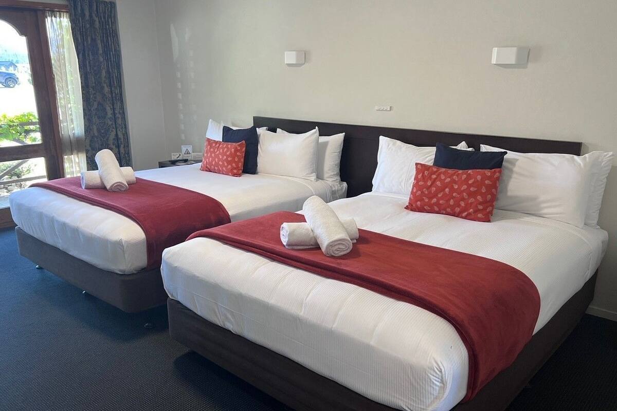 A hotel room with two beds, each with white linens and red accents, including pillows and a blanket.