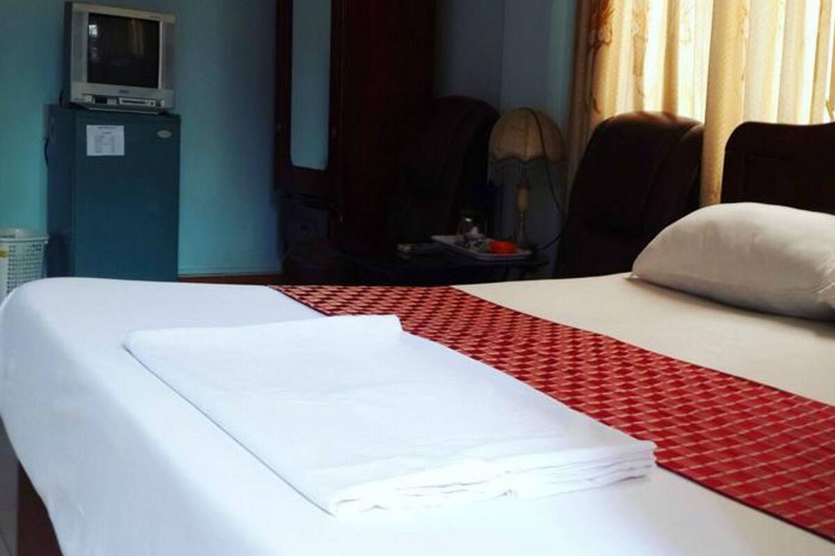 Una habitación de hotel con una cama bien hecha, un televisor sobre un mueble y una ventana con cortinas.