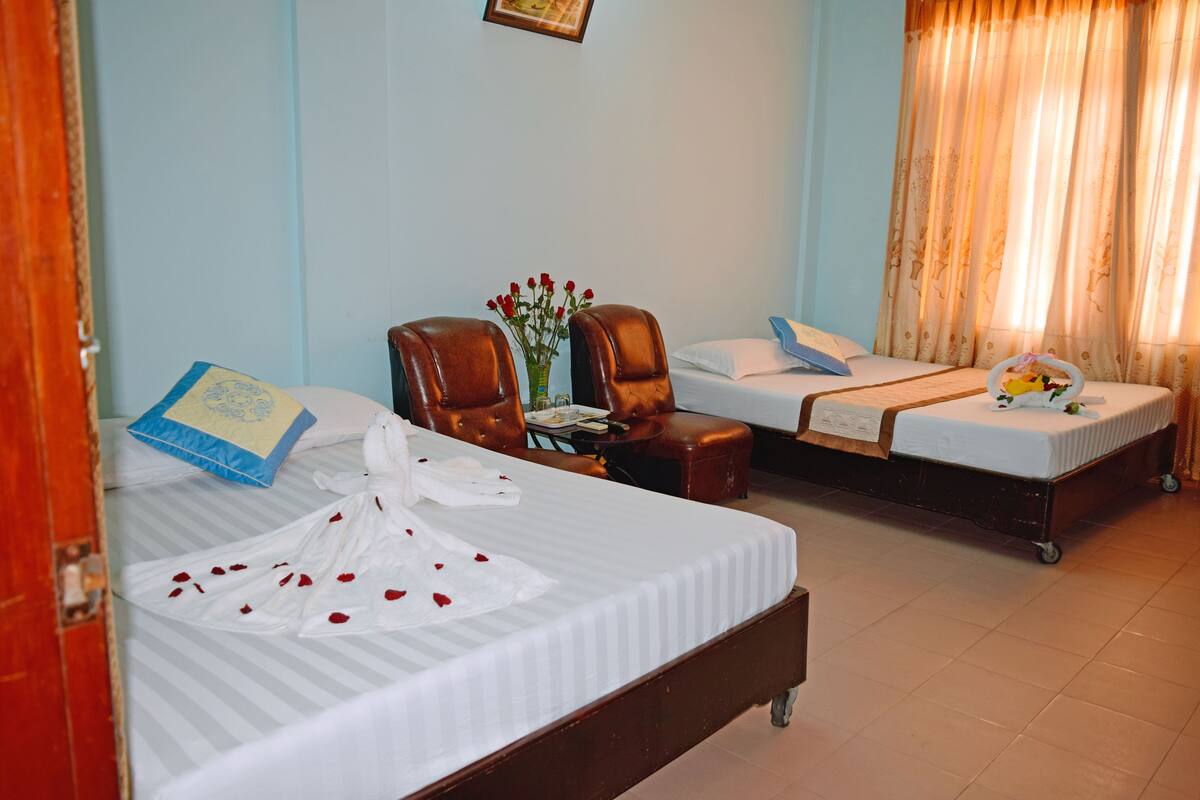 Habitación de hotel con dos camas, una mesita con un florero y un banco de madera.