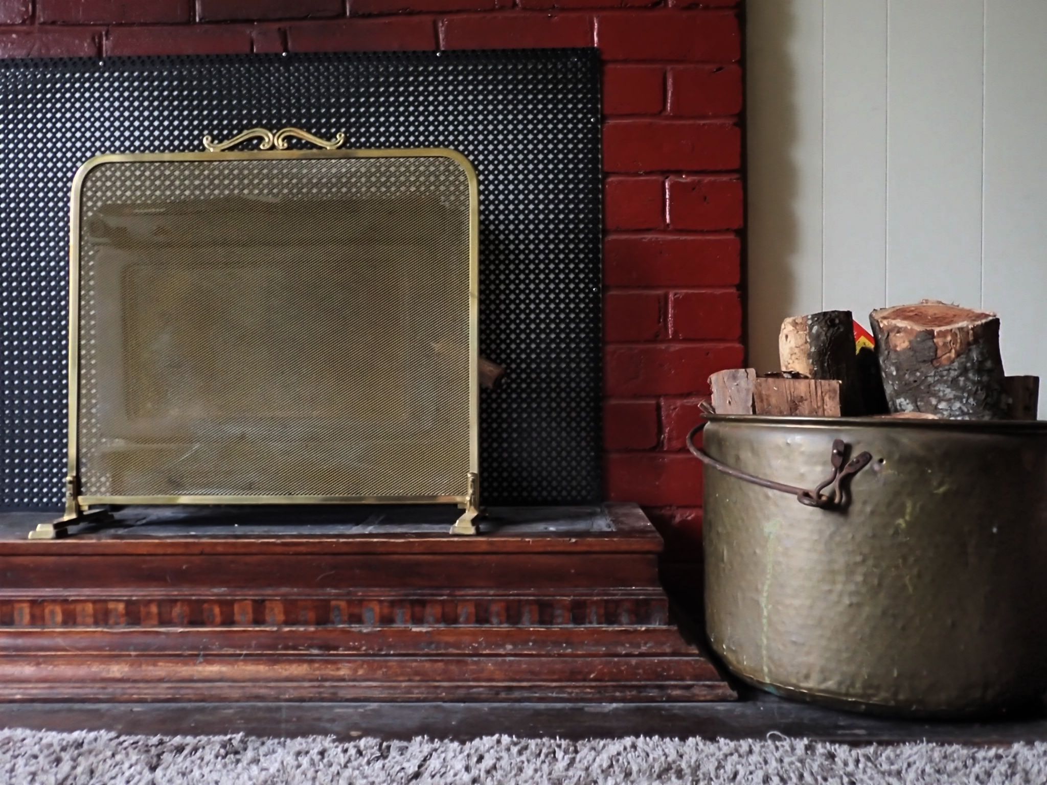 A fireplace with a metal screen, a wooden mantel, and a metal pot with logs.