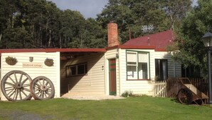 A cottage with a red roof, wooden wheelbarrows, and a sign reading "Glenbrook Cottage." - Glenbrook House and Cottage (Penguin)