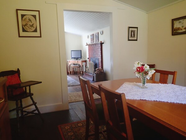 A dining area with a wooden table, chairs, and a vase of flowers. There is a television and a fireplace in the background.