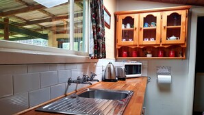 A kitchen with a wooden countertop, stainless steel sink, and a microwave. There are wooden cabinets above the counter with red containers. - Glenbrook House and Cottage (Penguin)