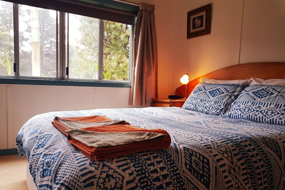 A neatly made bed with patterned bedding, a bedside lamp, and a window with curtains.