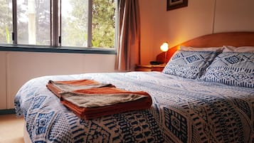 A neatly made bed with patterned bedding, a bedside lamp, and a window with curtains.