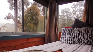 A bedroom with a bed, a window, and a view of trees. - Glenbrook House and Cottage (Penguin)