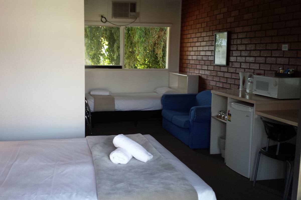 A hotel room with a bed, a small desk, a microwave, and a blue chair.