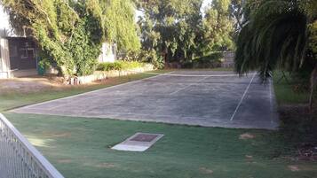 Una cancha de tenis al aire libre con un área verde circundante y árboles.