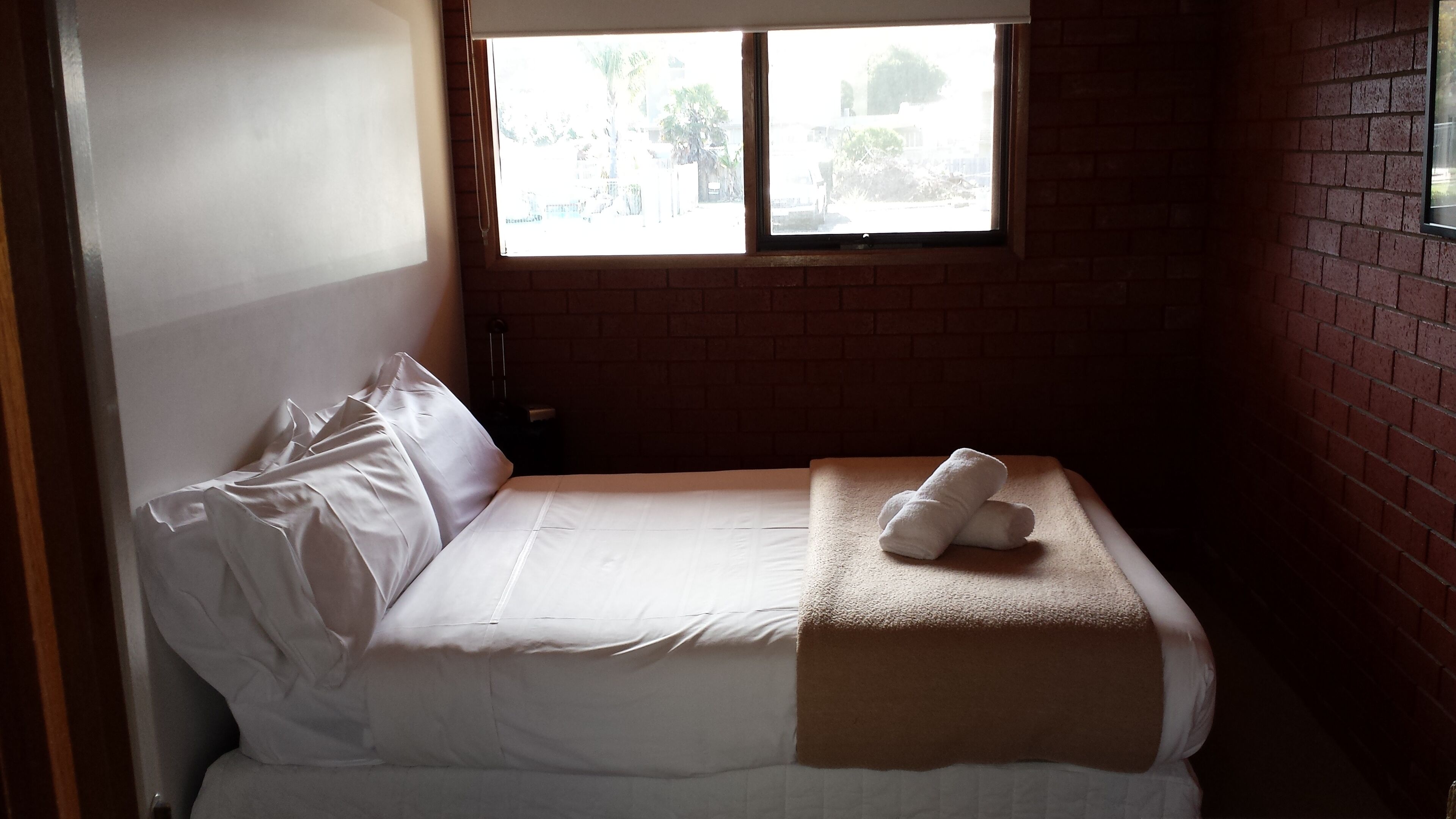 Uma cama de casal com lençóis brancos, janela com vista para o exterior e parede de tijolos.