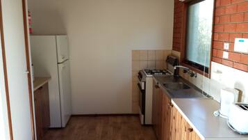 Cocina compacta con refrigerador, estufa, lavamanos y ventana con vistas al exterior.