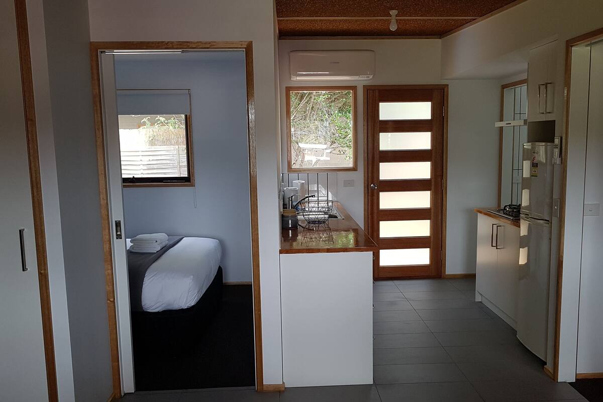 A compact hotel room with a bed, a small kitchenette, and a view through a window.