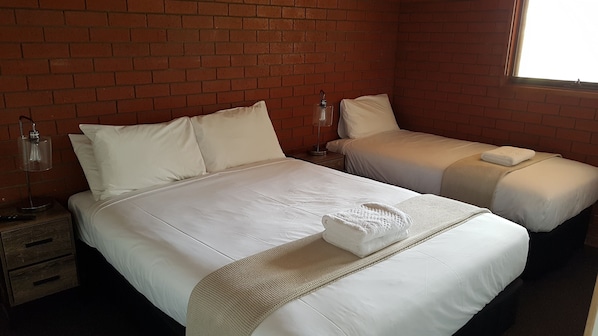 A hotel room with two single beds, a brick wall, a window, and a nightstand with a lamp.