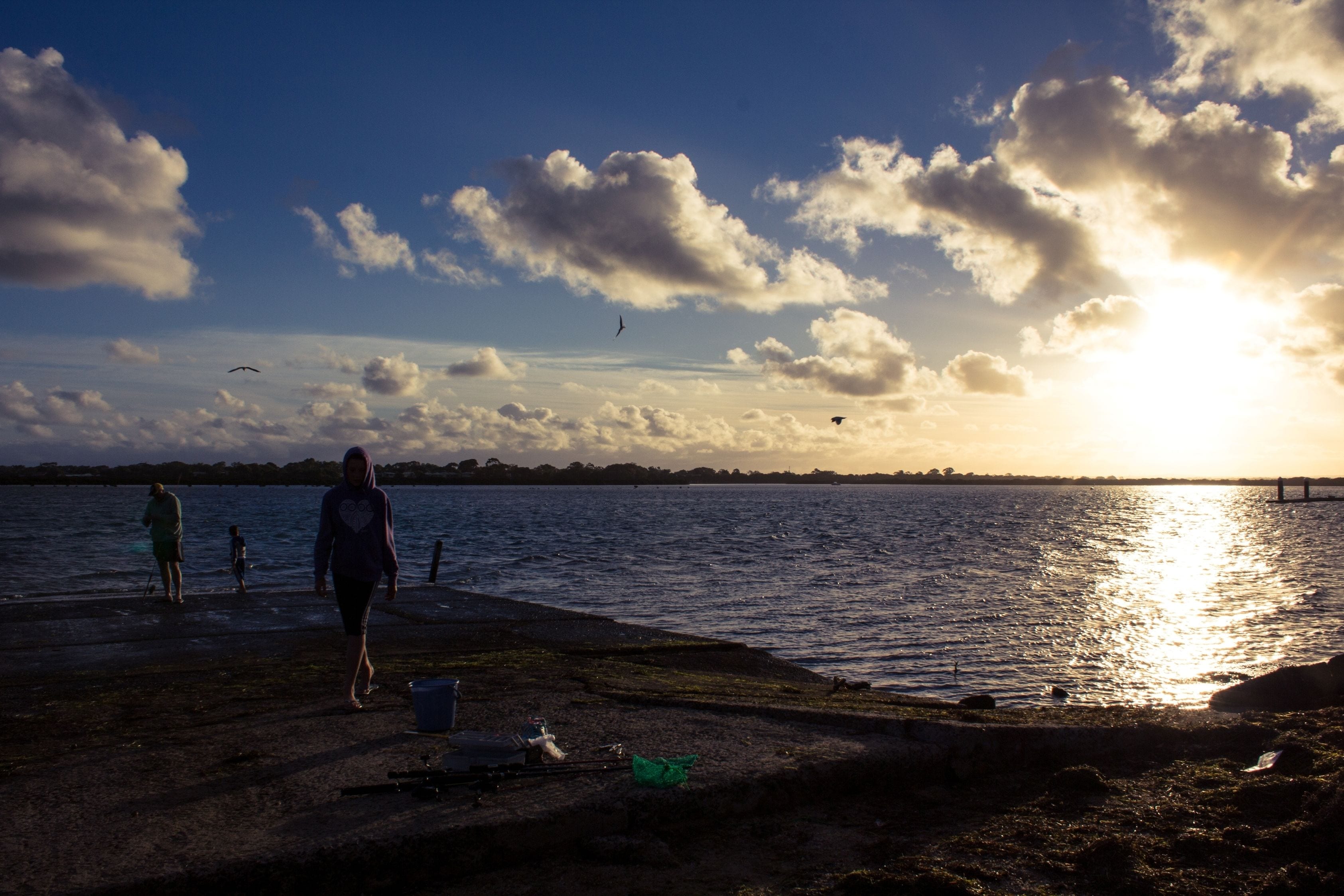 A waterfront scene with a sunset, a pier, and people walking along the shore.