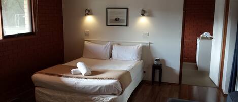 Un dormitorio con cama, una mesita de noche pequeña, un cuadro en la pared y una ventana.