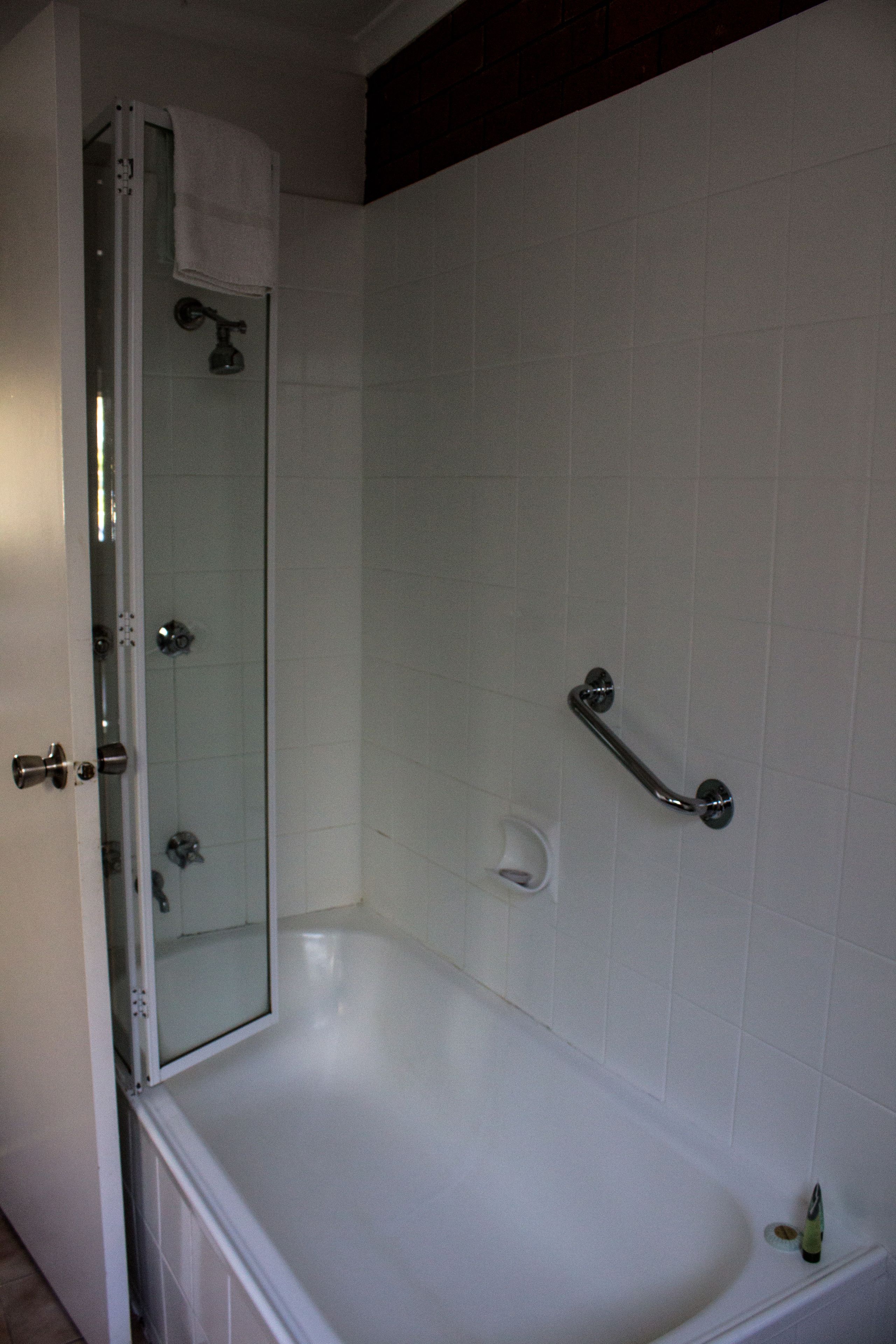 Une salle de bain avec une douche à parois de verre, une baignoire blanche et une barre d’appui.
