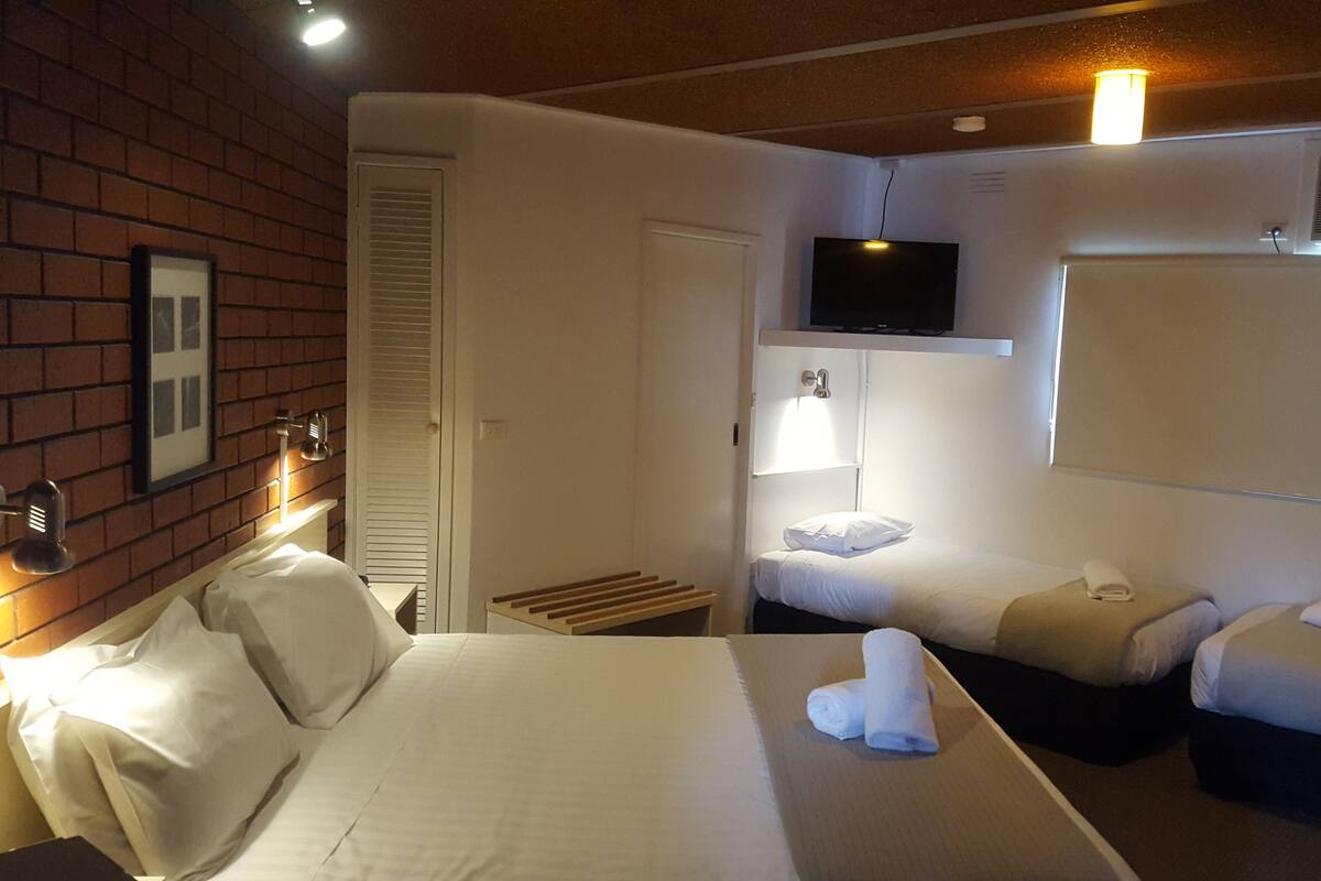 A hotel room with a large bed, two smaller beds, a TV mounted on the wall, and a brick wall.