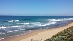 Una playa con olas, cielo despejado y una costa distante.