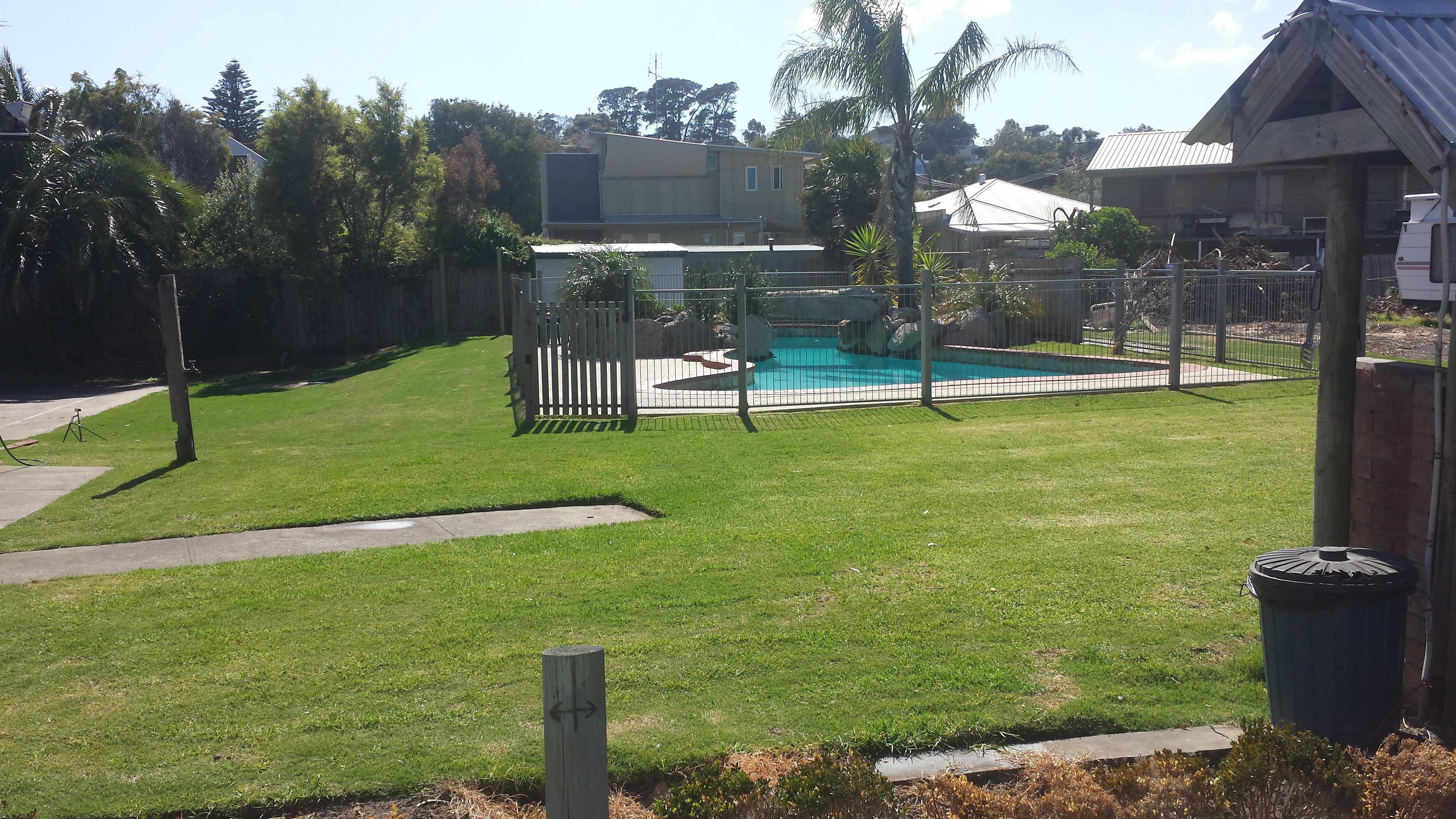 A backyard with a swimming pool, a wooden fence, and a grassy lawn.