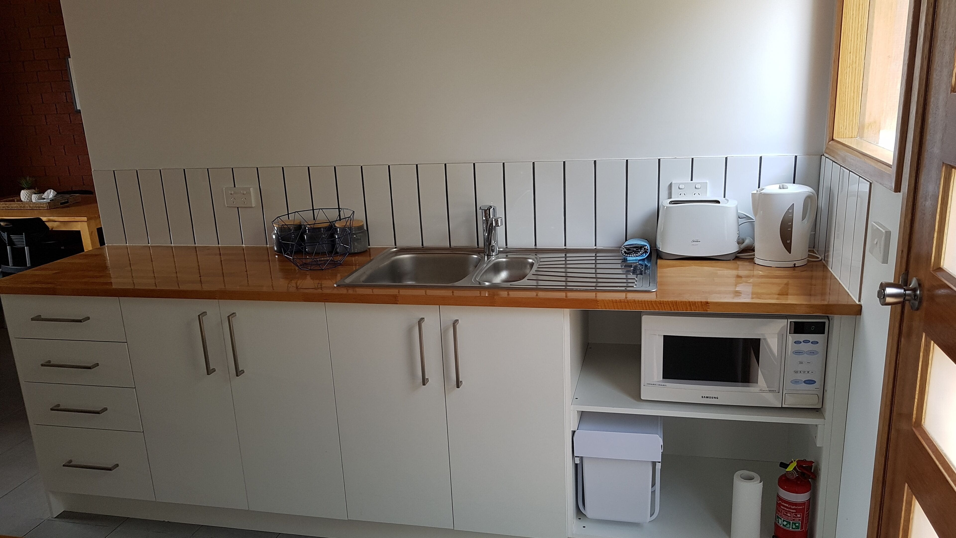 A kitchen with a wooden countertop, a sink, a microwave, and a toaster.