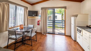 Una habitación con una mesa de comedor, sillas, televisor y una cocina con refrigerador, además de una puerta corrediza de vidrio que da a un espacio exterior.